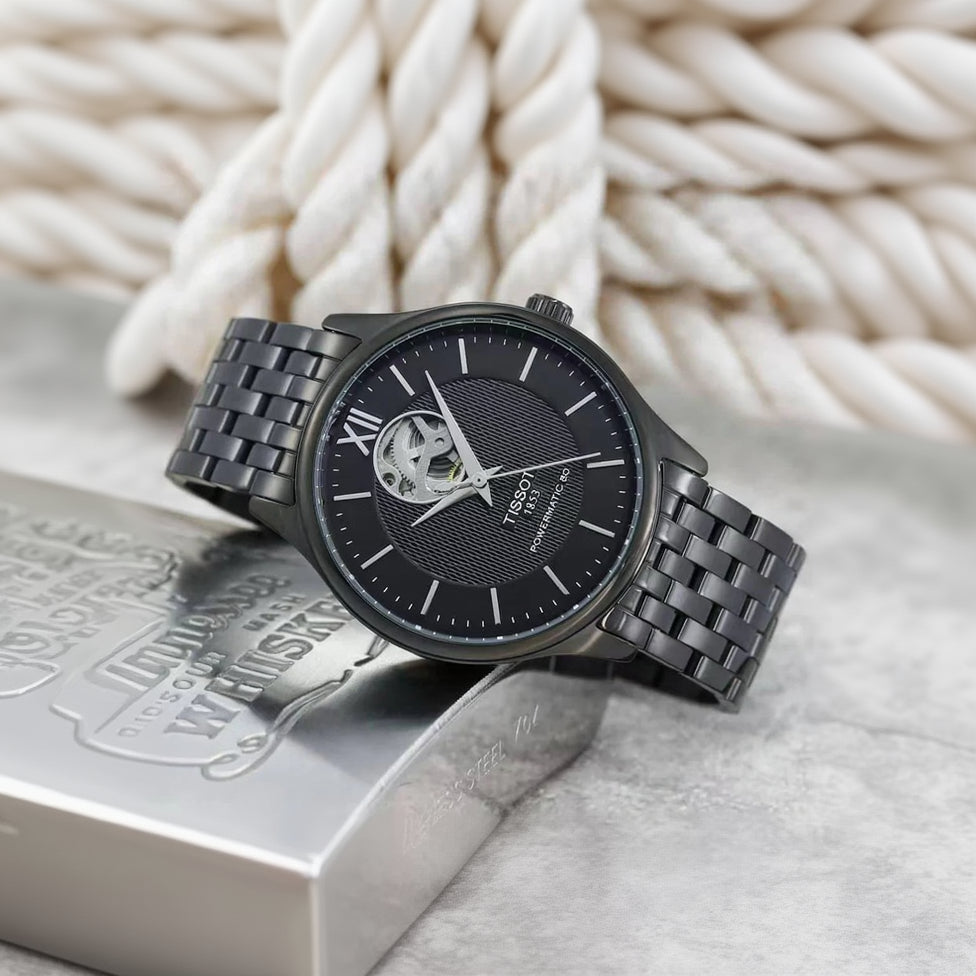 Black Tissot watch with metal strap on a textured surface